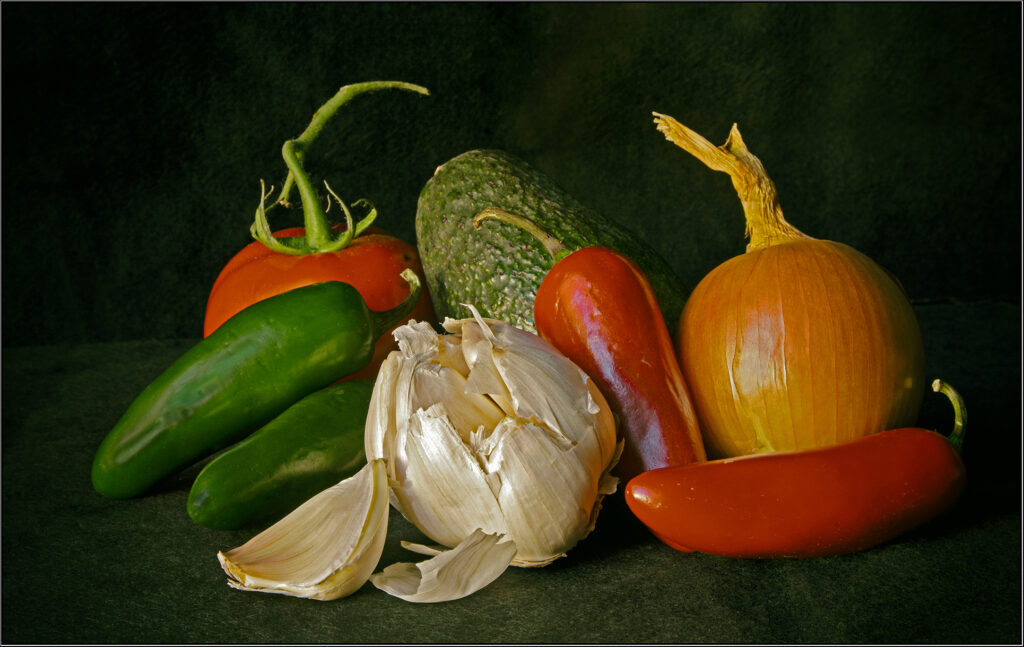 Photo of a peeling onion, two red peppers, 2 green peppers, a tomato, and other vegetables